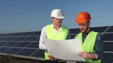 İki mühendis güneş panellerinin yanında duruyor. Bölgeyi inceliyorlar ve projeyi kontrol ediyorlar. 4K