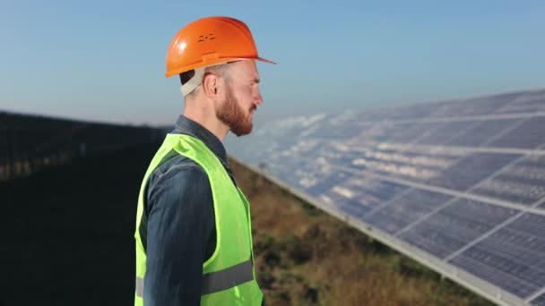 Inženýr prochází kolem solárních panelů. Má na sobě vestu a tvrdý klobouk. 4K — Stock video
