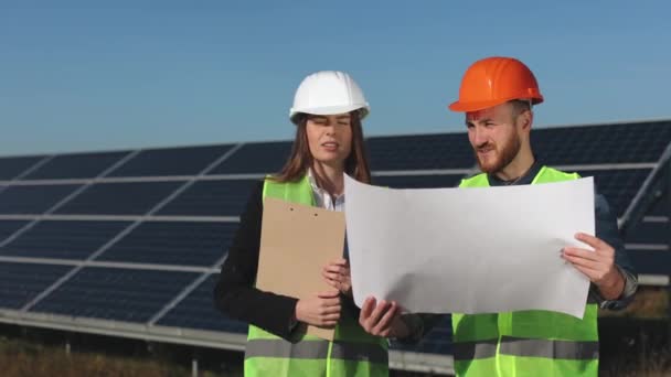 İki mühendis proje için çizimleri tartışıyor. Bir güneş paneli istasyonunda duruyorlar. 4K — Stok video