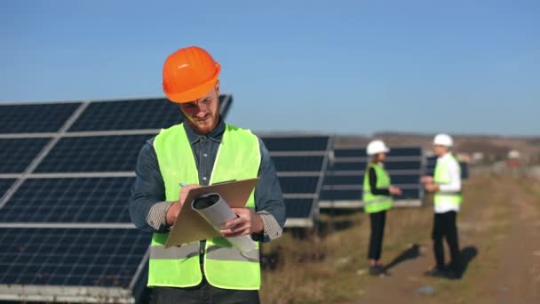 Inženýr kontroluje solární panely. Dva inženýři mluví v pozadí. 4K — Stock video