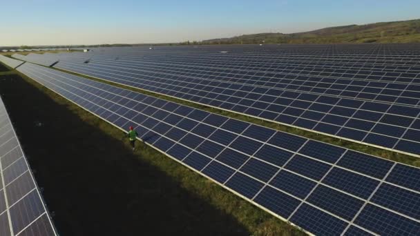Drone güneş paneli istasyonu vuruyor. Güneş panellerinden bir mühendis geçiyor. 4K — Stok video