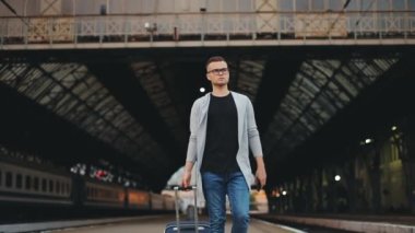 Bir adam istasyon platformunda yürüyor. Elinde bir bavul tutuyor. 4K