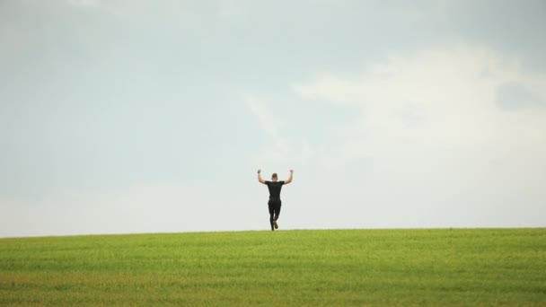 Si olahragawan berlari di rumput hijau dan melompat. Dia senang dan mengangkat tangannya di udara. Latihan lari. 4K — Stok Video