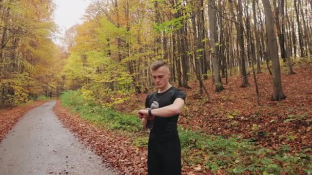 Der Sportler steht auf einem Waldweg und überprüft die Trainingsdaten auf der Sportuhr. Lauftraining im Herbstwald. 4K — Stockvideo