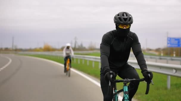 Twee atleten trainen op een fiets. Ze rijden op de snelweg. Training in het koude seizoen. 4K — Stockvideo