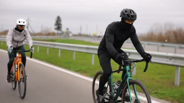 Twee atleten trainen op een fiets. Ze zijn gekleed in warme kleren en trainen in de tuin. Koud seizoen. 4K — Stockvideo