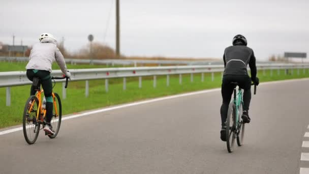Δύο αθλητές προπονούνται με ποδήλατο. Τελειώνουν την προπόνηση τους και ένας από αυτούς είναι καβάλα και κρατάει ψηλά τα χέρια του. Προπόνηση στην κρύα εποχή. Πυροβολισμός από πίσω. 4K — Αρχείο Βίντεο