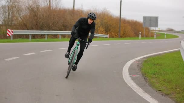 De sporter traint op de fiets. Hij gaat de bocht in met snelheid. Training in het koude seizoen. 4K — Stockvideo