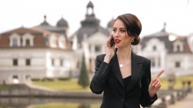 Genç bir kadın gidiyor ve duygusal olarak akıllı telefonuyla konuşuyor. O şık giyinmiş. Arka planda güzel bir mimari var. 4K