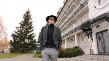 Adam yürüyor ve ileriye bakıyor. Şık giyinmiş. Arkadaki bina çok güzel. 4K