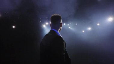 Takım elbiseli bir adam sahneye çıkıyor. Işıklar onun üzerinde parlıyor. O mutlu ve elini sallıyor. Konuşmacı konuşması. 4K