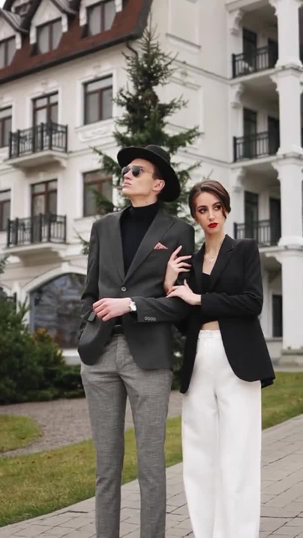 Ein Mann und eine Frau stehen da und schauen in die Natur. Sie kleiden sich in modische Kleidung. Schönes Gebäude im Hintergrund. Vertikales Video. — Stockvideo