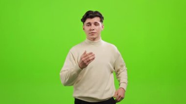 Adam ayakta duruyor ve kameraya bakıyor. Öpücük yolluyor. O, yeşil bir arka planın üzerinde duruyor. Yeşil ekran. 4K