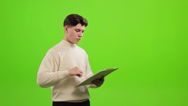 그 남자는 서서 카메라를 보고 있습니다. 서류를 뒤적거리고 있어요. 그는 푸른 배경 위에 서 있다. 녹색 화면. 4K — 비디오