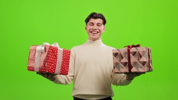 Ο άνθρωπος στέκεται και κοιτάζει την κάμερα. Γελάει και κρατάει δύο δώρα. Στέκεται πάνω σε ένα πράσινο φόντο. Πράσινη οθόνη. 4K — Αρχείο Βίντεο