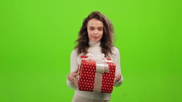 그 여자는 서서 카메라 를 보고 있다. 너한테 선물을 주는 거야. 그녀는 녹색 배경 위에 서 있습니다. 녹색 화면. 4K — 비디오
