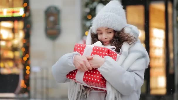 女が立って大きな贈り物を抱きかかえている。彼女は彼にとても満足している。彼女は笑っている。雪が降っている。4K — ストック動画