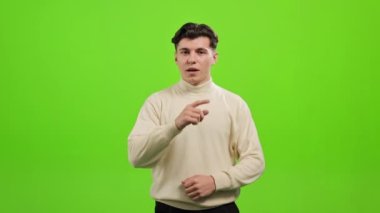 Adam ayakta duruyor ve kameraya bakıyor. O, parmağını ağzına koyuyor ve sessizce işaret ediyor. O, yeşil bir arka planın üzerinde duruyor. Yeşil ekran. 4K