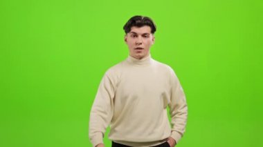 Adam ayakta duruyor ve kameraya bakıyor. Elini kaldırıyor ve el sallıyor. Hayır. O, yeşil bir arka planın üzerinde duruyor. Yeşil ekran. 4K