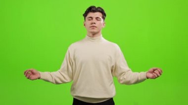 Adam ayakta duruyor ve kameraya bakıyor. Ellerini kaldırıyor ve gözleri kapalı meditasyon yapıyor. O, yeşil bir arka planın üzerinde duruyor. Yeşil ekran. 4K