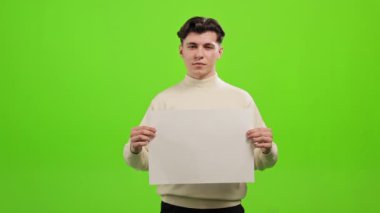 Adam ayakta duruyor ve kameraya bakıyor. O, beyaz bir kağıt tutuyor. O, yeşil bir arka planın üzerinde duruyor. Yeşil ekran. 4K