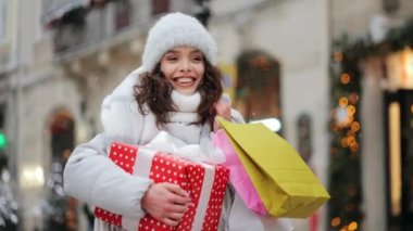Kar yağışı sırasında bir kadın şehir merkezine gidiyor. Elinde büyük bir hediye ve alışveriş poşetleri var. O gülümsüyor. Portre çekimi. 4K