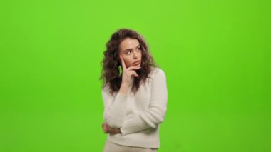 Kadın ayakta duruyor ve düşünüyor. O, elini çenesine dayıyor. O, yeşil bir arka planın üzerinde duruyor. Yeşil ekran. 4K