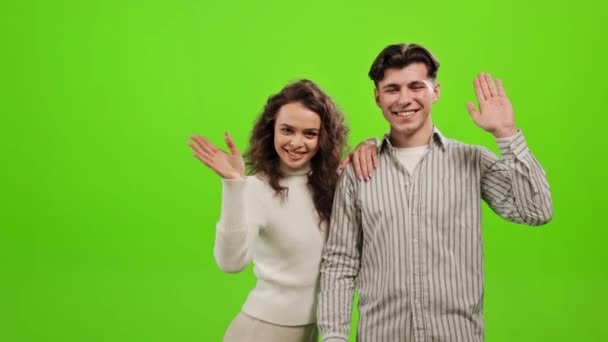 Ένας άντρας και μια γυναίκα στέκονται και κοιτάζουν την κάμερα. Χαιρετούν και χαμογελούν. Στέκονται σε ένα πράσινο φόντο. Πράσινη οθόνη. 4K — Αρχείο Βίντεο