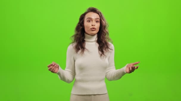 Η γυναίκα στέκεται και κοιτάζει την κάμερα. Κουνάει τα χέρια της και μιλάει. Στέκεται πάνω σε ένα πράσινο φόντο. Πράσινη οθόνη. 4K — Αρχείο Βίντεο