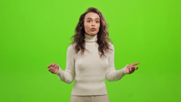 La mujer está de pie y mirando a la cámara. Ella agita las manos y habla. Está de pie sobre un fondo verde. Pantalla verde. 4K — Vídeos de Stock