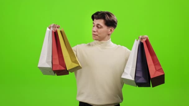 El hombre está parado y sosteniendo las bolsas de la compra. Él está mirando a la cámara y sonriendo. Está de pie sobre un fondo verde. Pantalla verde. 4K — Vídeo de stock