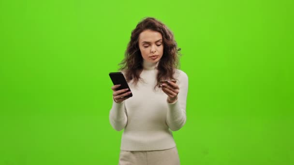 Η γυναίκα εισάγει τα στοιχεία της κάρτας της στο κινητό της. Πληρώνει για την αγορά. Στέκεται πάνω σε ένα πράσινο φόντο. Πράσινη οθόνη. 4K — Αρχείο Βίντεο