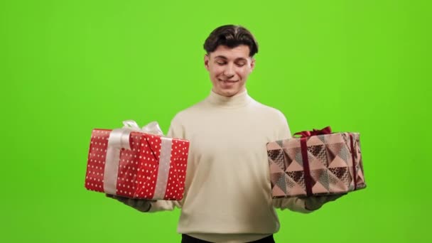 Mannen står och tittar på kameran. Han håller två stora presenter och ler. Han står på en grön bakgrund. Grön skärm. 4K — Stockvideo