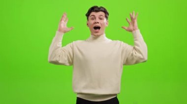 Adam ayakta duruyor ve kameraya bakıyor. Ellerini kaldırıyor ve çok şaşırmış görünüyor. Gülümsüyor. O, yeşil bir arka planın üzerinde duruyor. Yeşil ekran. 4K