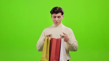Bir adam alışveriş torbalarına bakıyor. Gülümsüyor ve seviniyor. O, yeşil bir arka planın üzerinde duruyor. Yeşil ekran. 4K