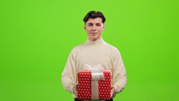 Ο άνθρωπος στέκεται και κοιτάζει την κάμερα. Κρατάει ένα μεγάλο κουτί δώρου. Στέκεται πάνω σε ένα πράσινο φόντο. Πράσινη οθόνη. 4K — Αρχείο Βίντεο