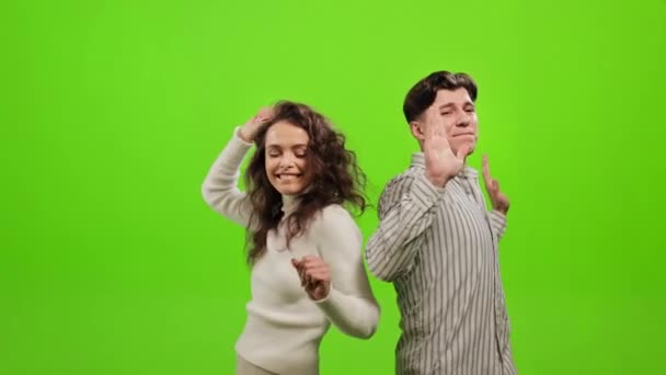 Ένας άντρας και μια γυναίκα ακούνε μουσική και χορεύουν. Χαμογελούν και διασκεδάζουν. Στέκονται σε ένα πράσινο φόντο. Πράσινη οθόνη. 4K — Αρχείο Βίντεο