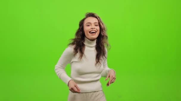 女は立ってカメラを見ている。彼女は指を折って踊っている。彼女は笑っている。彼女は緑の背景に立っている。緑の画面だ。4K — ストック動画