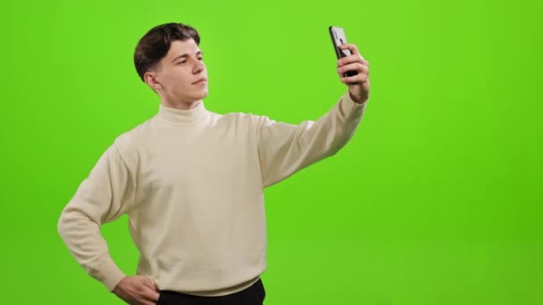 Um homem está a tirar uma selfie num smartphone. Ele está de pé sobre um fundo verde. Tela verde. 4K — Vídeo de Stock