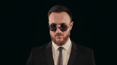 Takım elbiseli bir adam sahnede duruyor ve kameraya bakıyor. Güneş gözlüğü takıyor. O, şapkasını takıyor. Portre çekimi. 4K