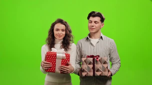 Ένας άντρας και μια γυναίκα κρατούν δώρα. Χαμογελάνε και κοιτάζονται. Στέκονται σε ένα πράσινο φόντο. Πράσινη οθόνη. 4K — Αρχείο Βίντεο