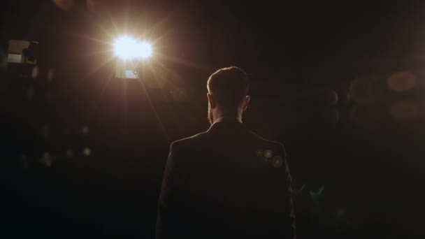 A man is standing on the stage and looking into the audience. He is dressed in a suit. The spotlight is shining on him. The speaker performs on stage. 4K — Stock Video