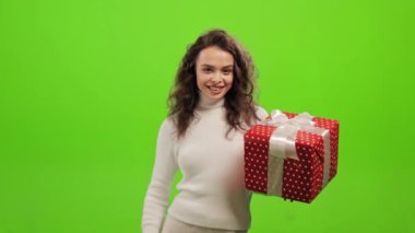 The woman is standing and looking at the camera. She is holding the gift and raising her finger up. She is standing on a green background. Green screen. 4K