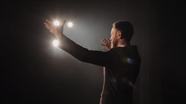 En mand optræder følelsesmæssigt på scenen. Han vifter med hænderne. Lyset skinner på ham. 4K – Stock-video