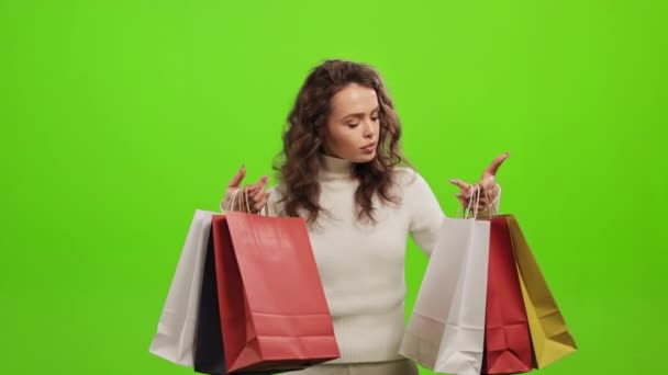 그 여자는 쇼핑백을 집어들어 살펴보고 있습니다. 머리를 들고 카메라를 보고 있습니다. 그녀는 녹색 배경 위에 서 있습니다. 녹색 화면. 4K — 비디오