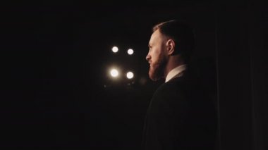 Bir adam sahnede duruyor ve seyirciye bakıyor. O bir takım elbise giydi. Spot ışıkları onun üzerinde parlıyor. Hoparlör sahnede çalıyor. Kamera geriye doğru hareket ediyor. 4K
