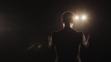 Bir adam sahnede duruyor ve ellerini çırpıyor. Gülümsüyor. Spot ışıkları onun üzerinde parlıyor. Kamera onun etrafında dönüyordu. 4K
