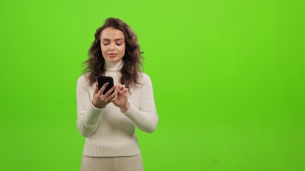 Η γυναίκα ψάχνει μέσω των κοινωνικών δικτύων στο smartphone της. Σηκώνει το κεφάλι της και κοιτάζει την κάμερα. Έχει μια ιδέα και σηκώνει το δάχτυλό της. Στέκεται πάνω σε πράσινο φόντο. — Αρχείο Βίντεο