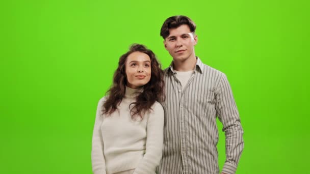 Ένας άντρας και μια γυναίκα στέκονται και κοιτάζουν την κάμερα. Είναι χαρούμενοι και χαμογελούν. Στέκονται σε ένα πράσινο φόντο. Πράσινη οθόνη. 4K — Αρχείο Βίντεο