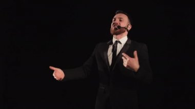 Adam sahnede duruyor ve duygusal olarak konuşuyor. O, ellerini sallıyor. Üzerinde bir mikrofon var. Takım elbise giyiyor. 4K